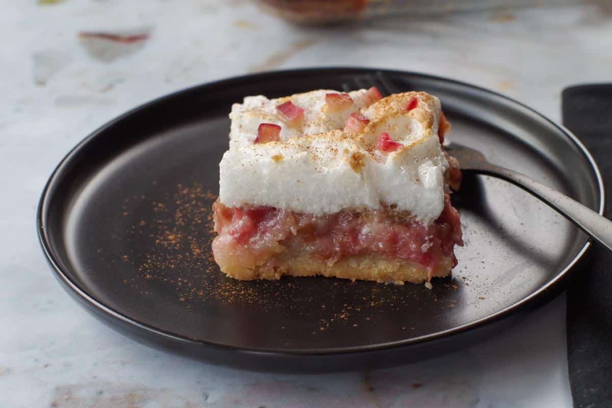 a piece of rhubarb meringue torte on a black plate with a fork
