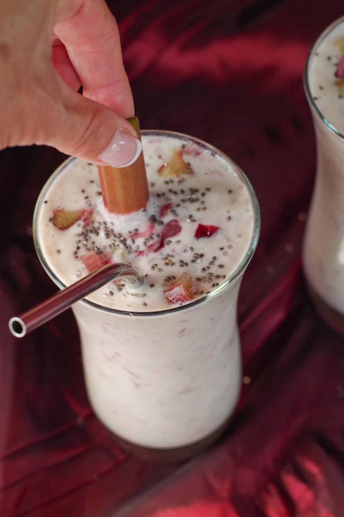 rhubarb smoothie with hand reaching for piece of rhubarb in smoothie