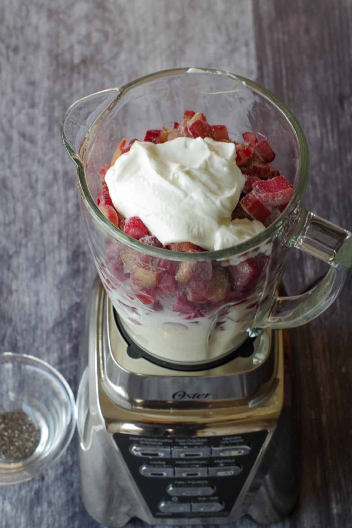 Rhubarb smoothie ingredients in the blender with a bowl of chia seeds on the side