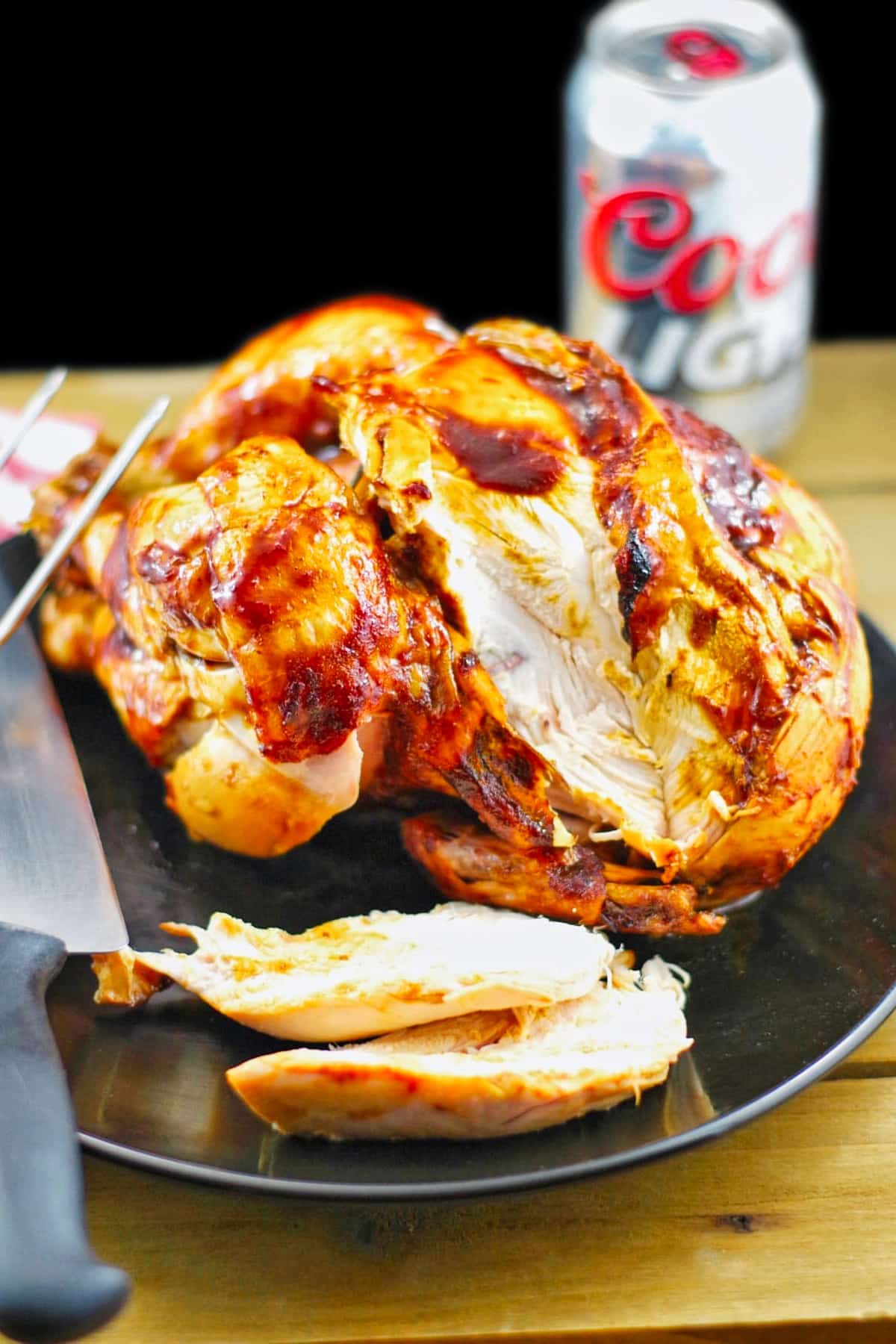 beer can chicken, sliced, on a black pate, with a knife, and a can of beer in the background