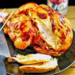 beer can chicken, sliced, on a black pate, with a knife, and a can of beer in the background