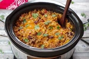 melted cheese and cilantro on cowboy casserole in crockpot, with a wooden spoon