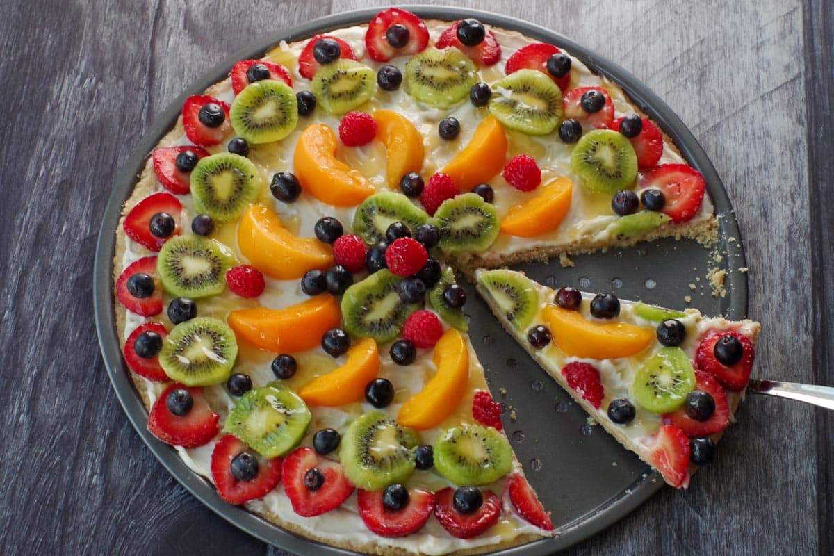 fruit pizza with a slice being lifted out