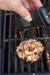 instant-read thermometer taking temperature of chicken burger on grill