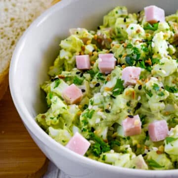 half a bowl of ham avocado and egg salad in a white bowl