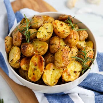 Rosemary Garlic Potatoes in a white bowl, with a blue and white striped linen underneath