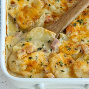 scalloped potatoes and ham in a white casserole dish, with a wooden spoon