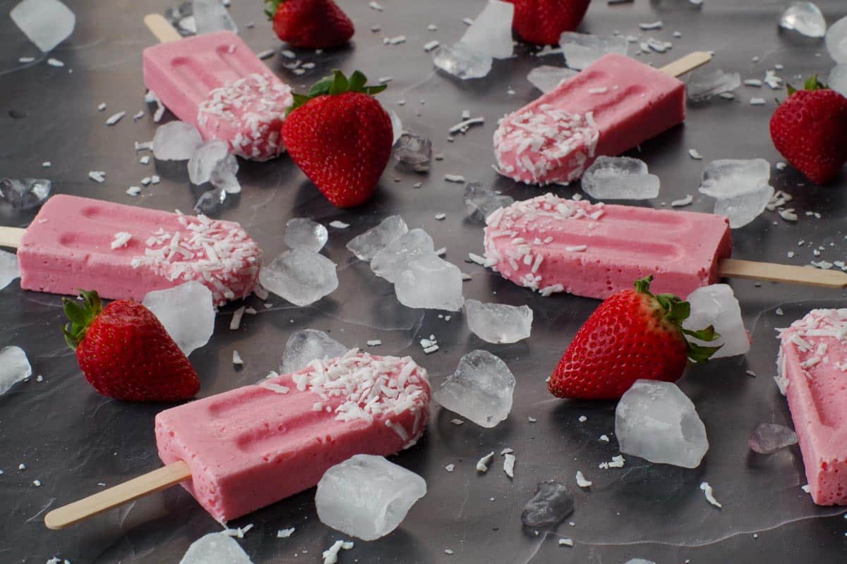 strawberry yogurt popsicles on a black counter surface with ice and fresh strawberries