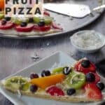 slice of fruit pizza on a white plate with a whole pizza on a pizza pan in the background