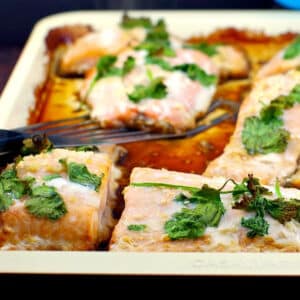 cooked salmon on a sheet pan, with a piece being lifted off with a stainless steel fish turner