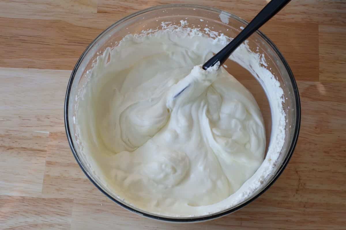 condensed milk mixed with whipped cream in a glass bowl, with black spatula