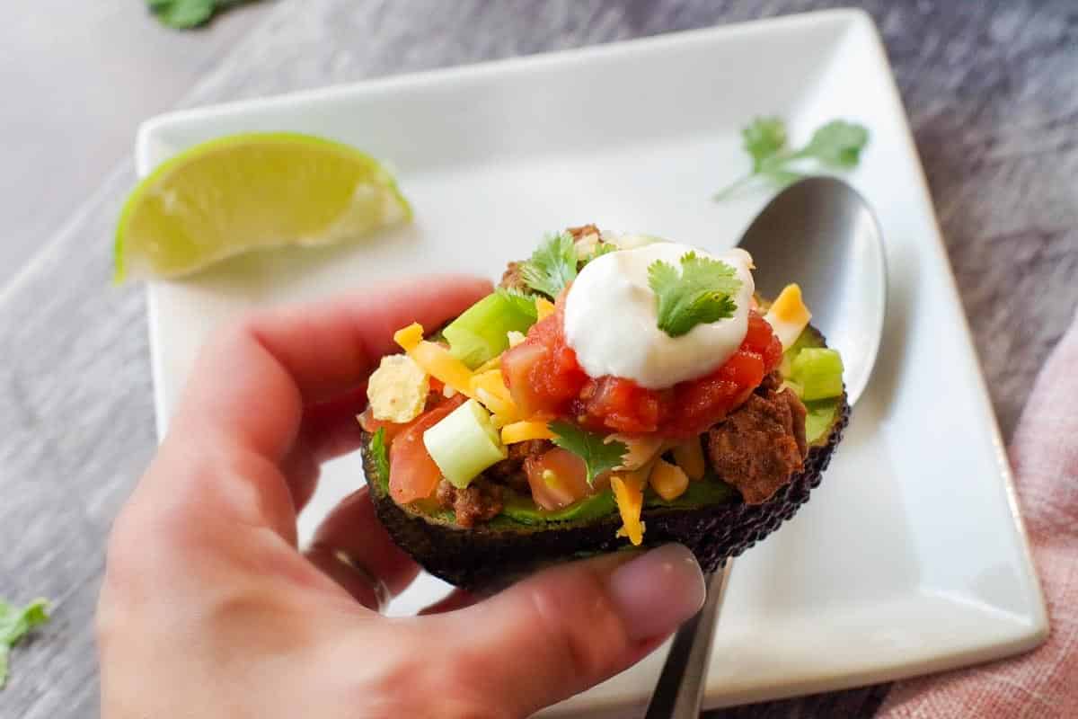 avocado taco being held up by a hand over a white plate