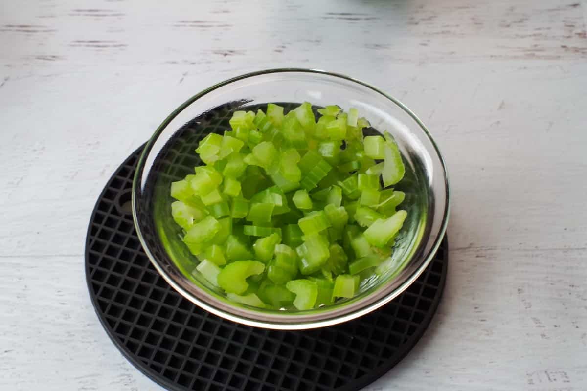 chopped, cooked celery in a glass bowl, with a black silicone trivet underneath