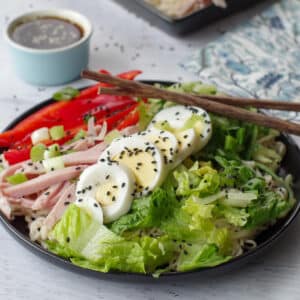 Japanese cold noodle salad on a black plate, with chopsticks and a dish of dressing in the background