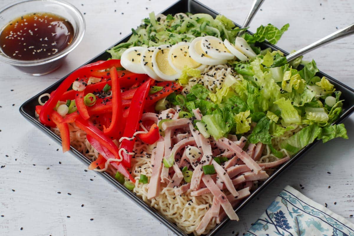 Japanese cold noodle salad on a black serving platter with a glass bowl of dressing on the side