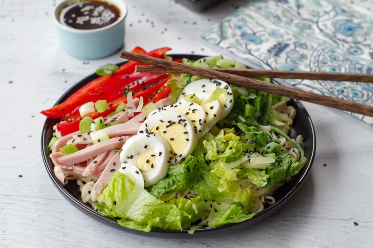 Japanese cold noodle salad on a black plate, with chopsticks and a dish of dressing in the background