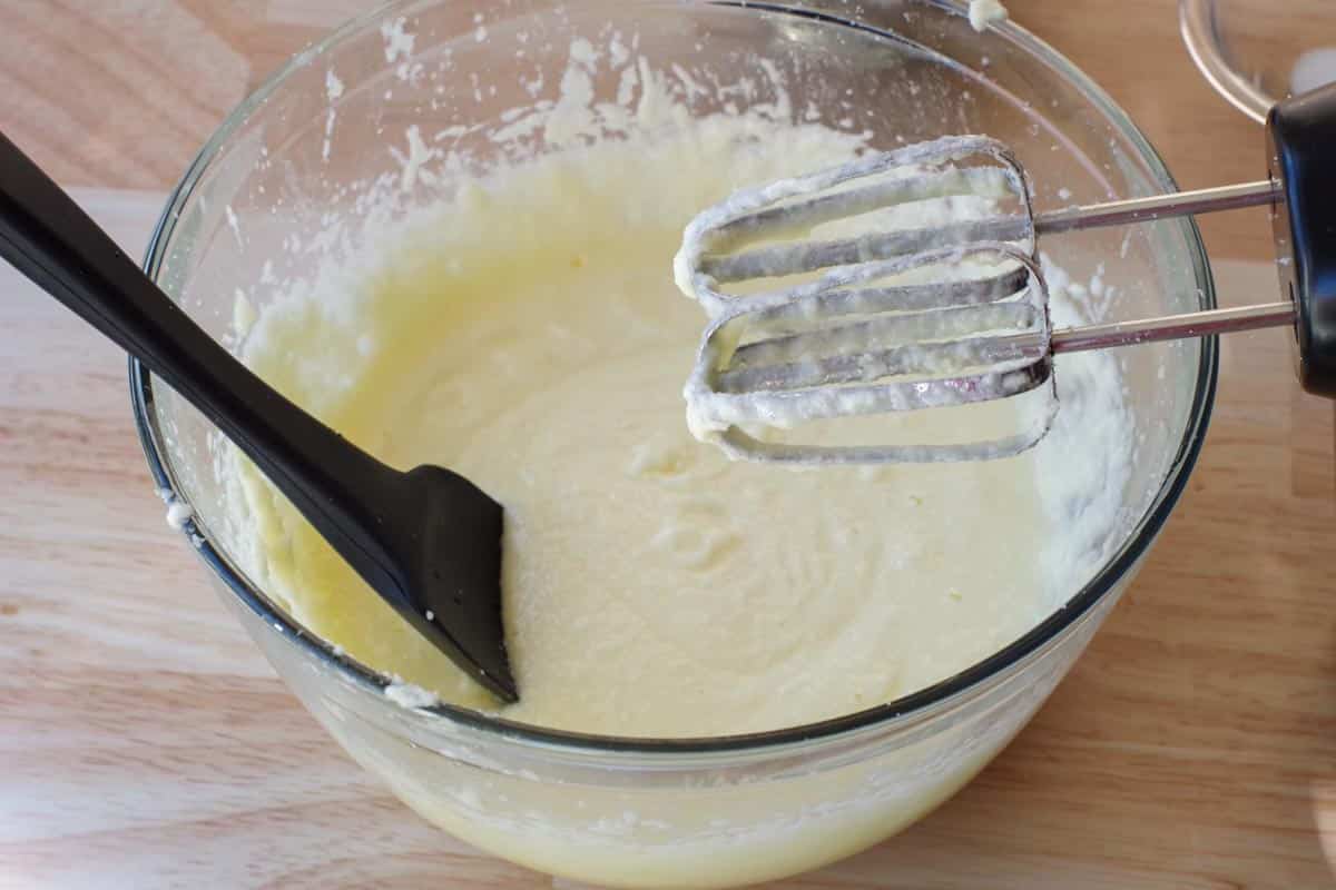 eggs added to butter sugar mixture, in glass mixing bowl with beater and black spatula
