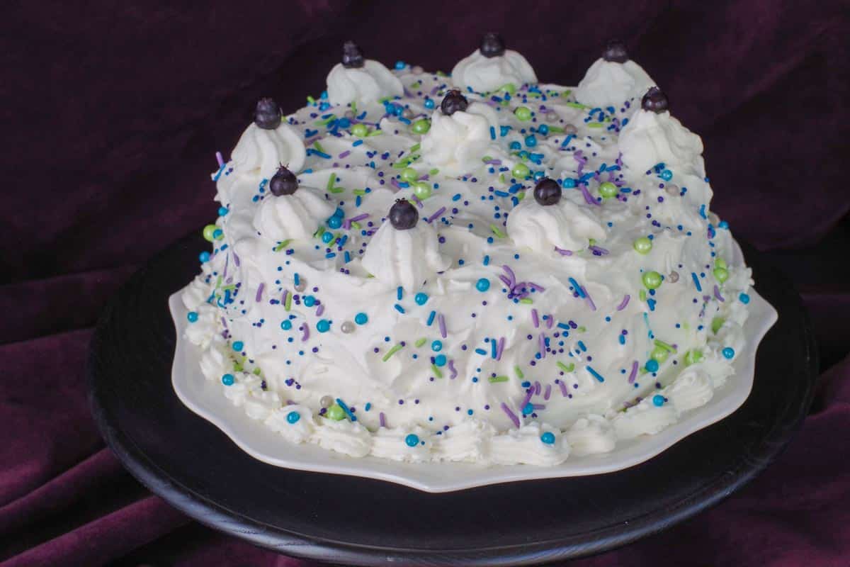 a whole Saskatoon berry cake, with white sprinkles on top, on a white plate on a black platter