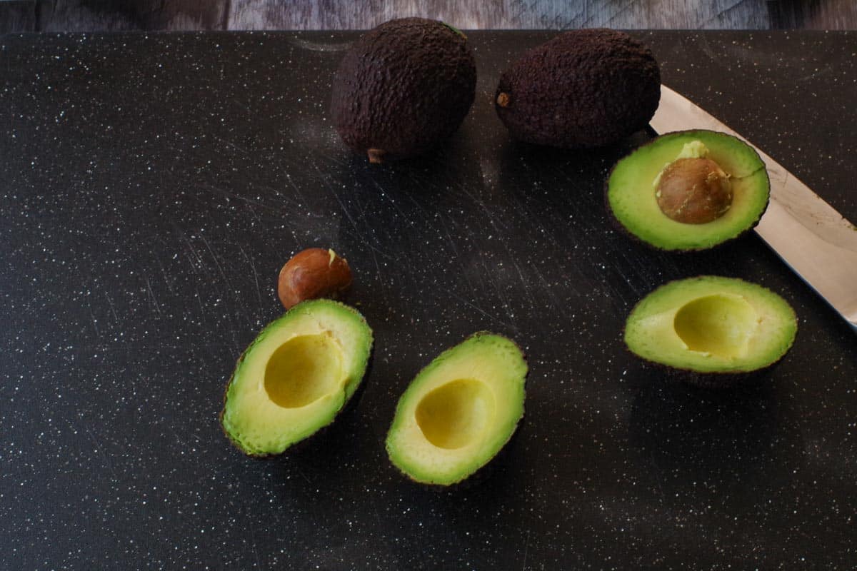 avocados cut in half on a black cutting board with a knife