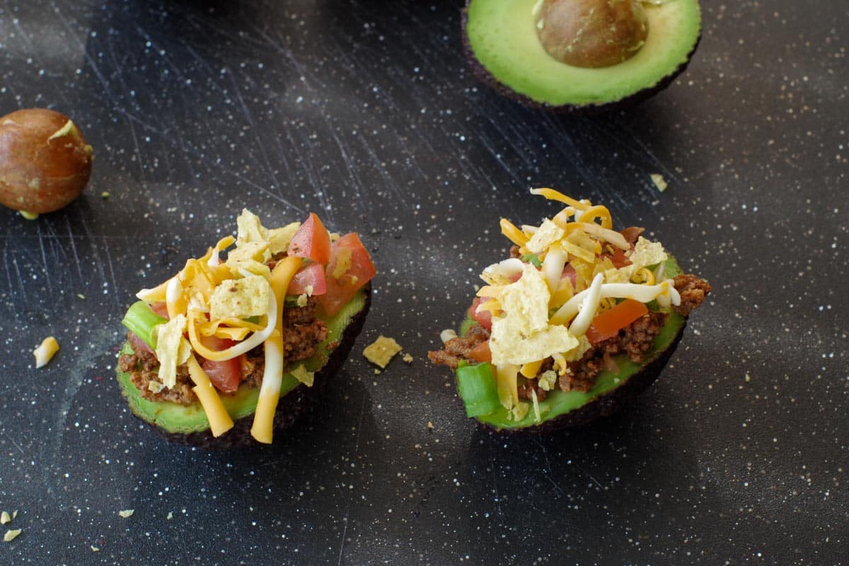 cheese and crunched up taco shell added to avocado tacos, on a black cutting board