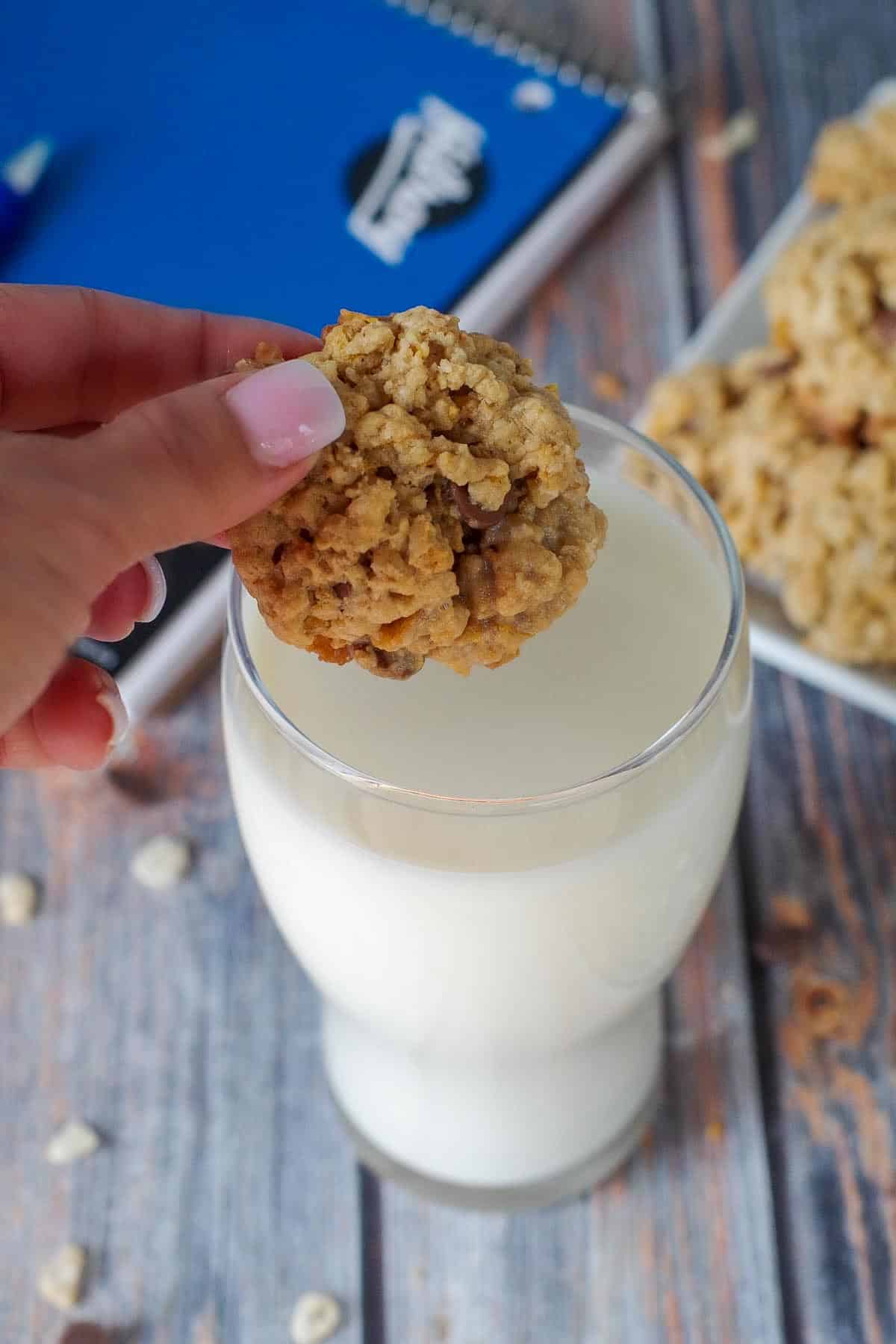 School Day cereal cookies being held over glass of milk with plate of cookies, milk and school binder in background