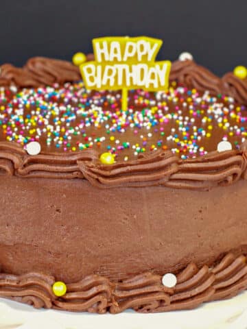 cake frosted with no butter chocolate frosting with sprinkles and Happy Birthday sign on top