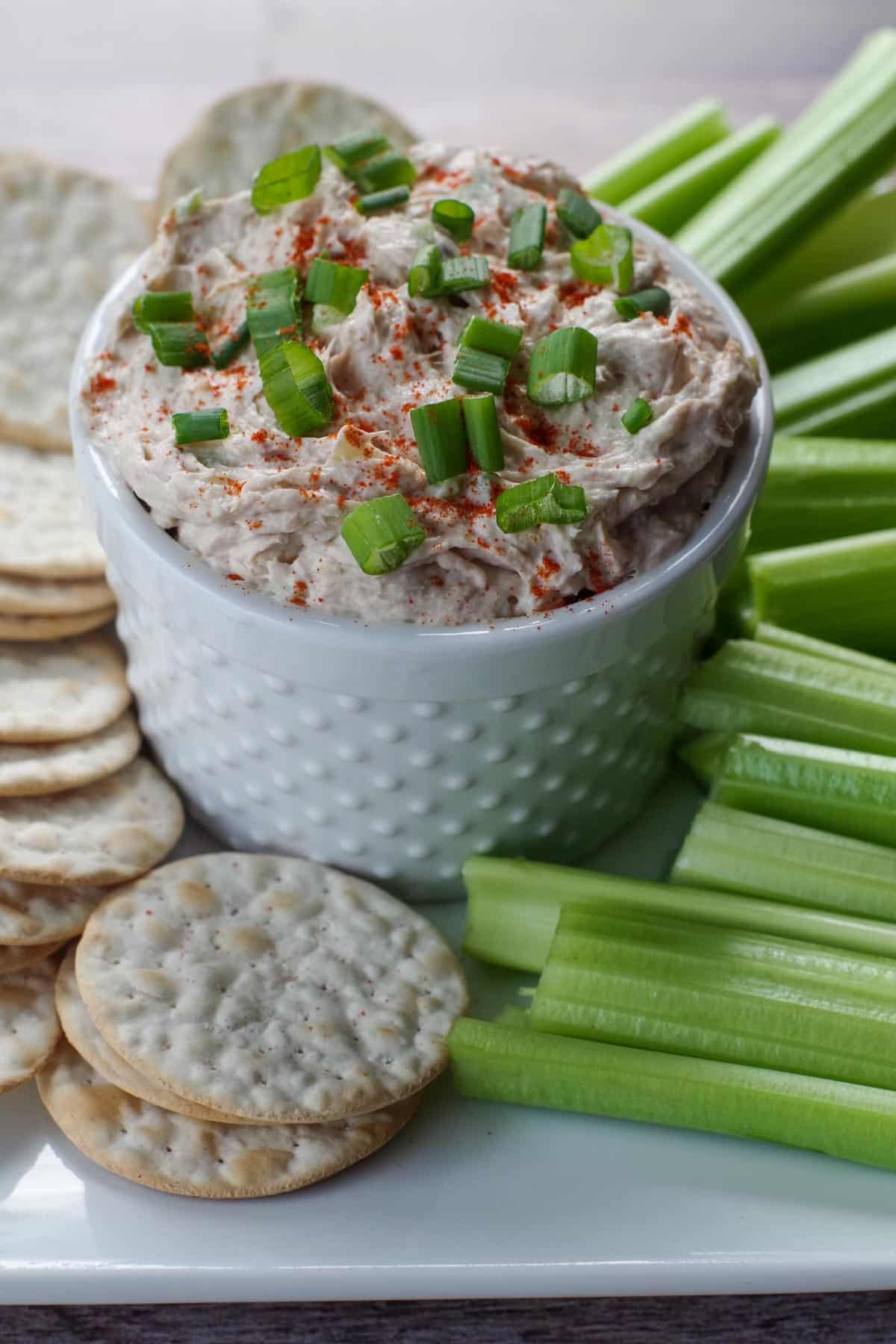 tuna dip in white container on a tray with crackers and celery