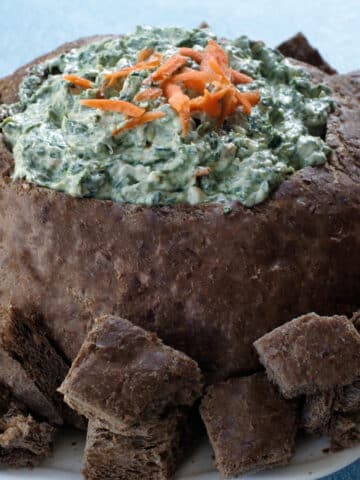 pumpernickel spinach dip bread bowl, surrounded by bread on a white plate