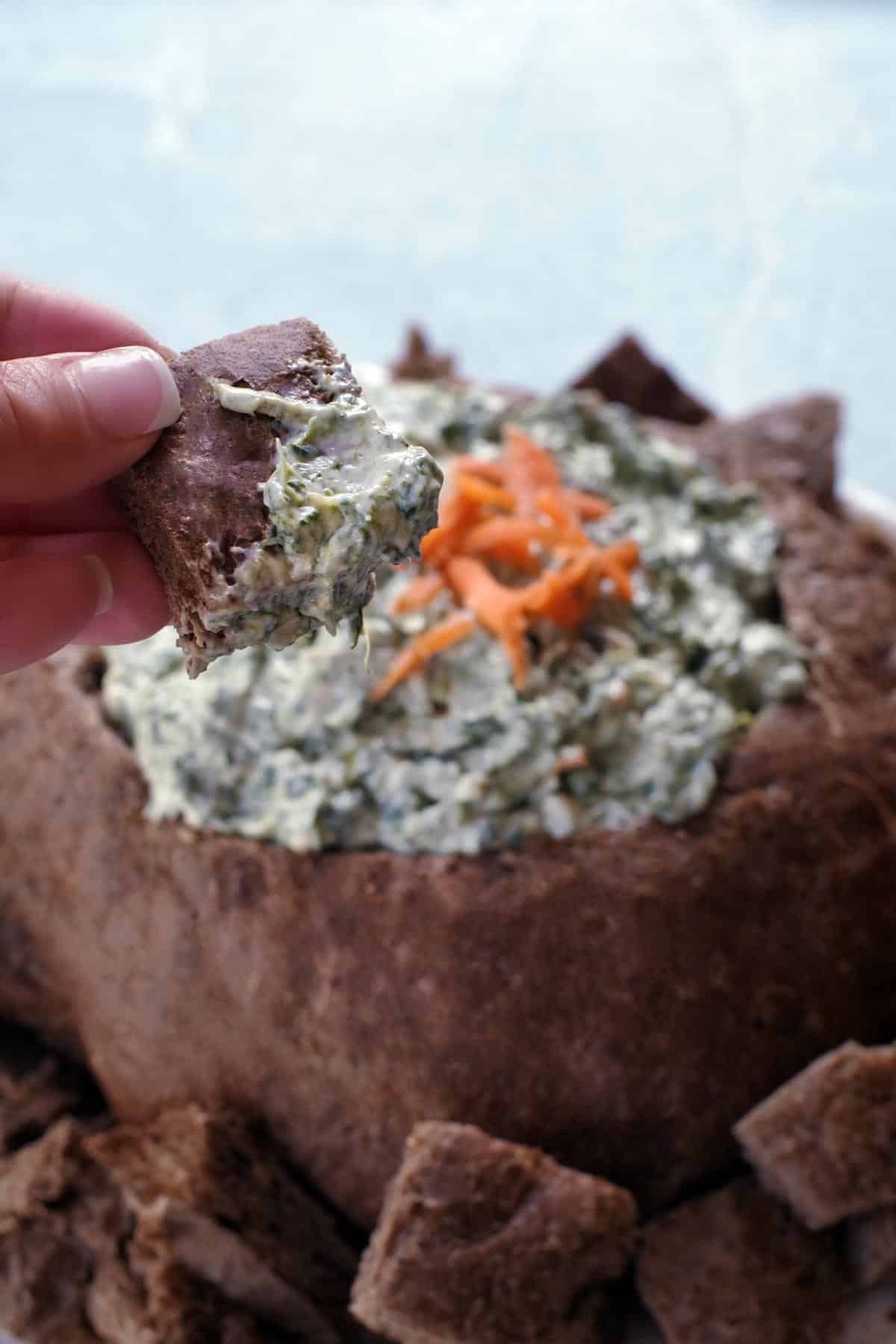 piece of bread being dipped into pumpernickel spinach dip