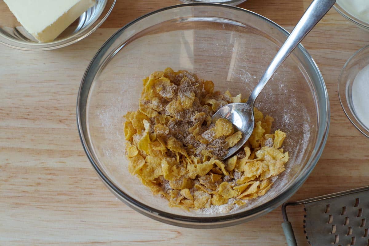 cornflakes mixed with brown sugar and flour in glass bowl with spoon