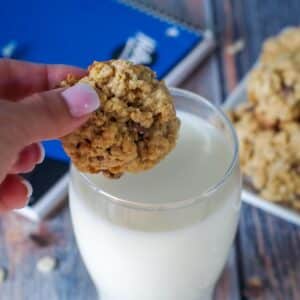 School Day cereal cookies being held over glass of milk with plate of cookies, milk and school binder in background