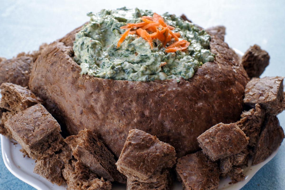 pumpernickel spinach dip bread bowl, surrounded by bread on a white plate