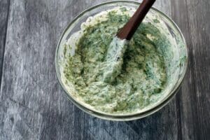 Ingredients in pumpernickel spinach dip mix together in glass bowl with wooden spoon