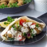 air fryer falafel pita on a black plate with a bowl of falafel balls in the background