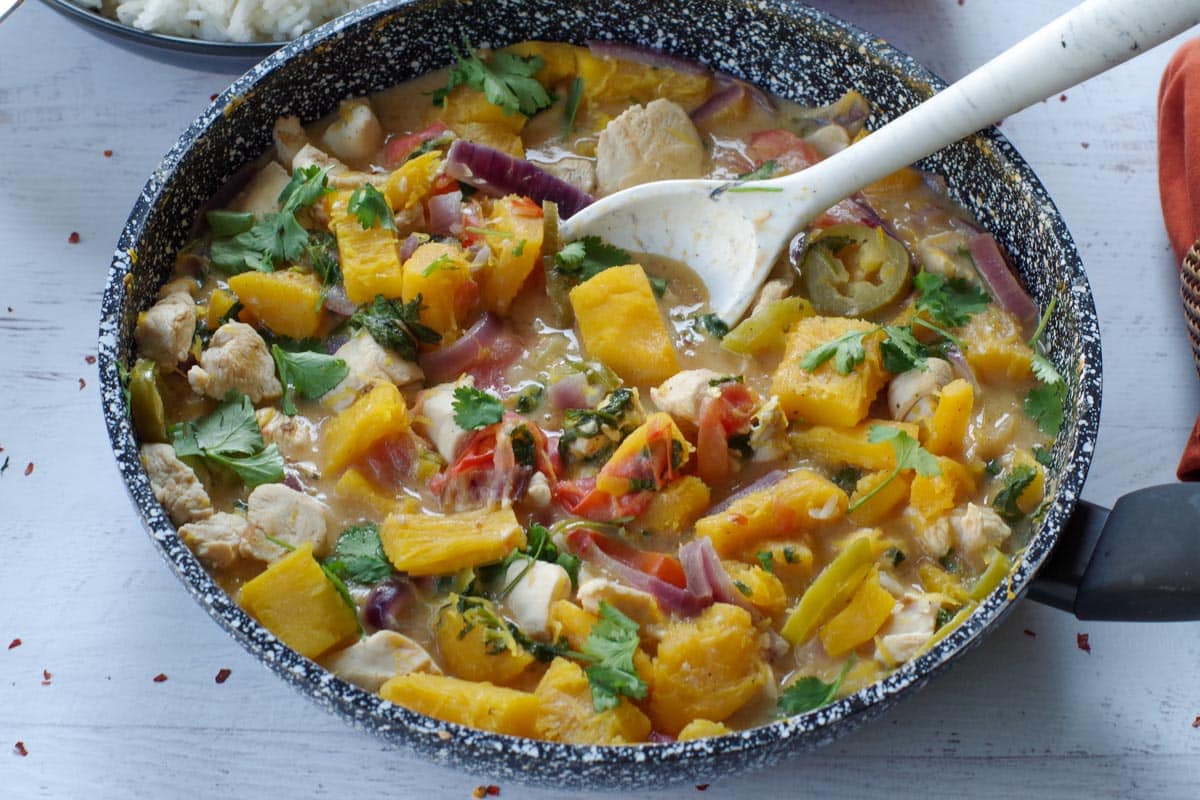 coconut pumpkin chicken in a frying pan with a marble patterned white serving spoon