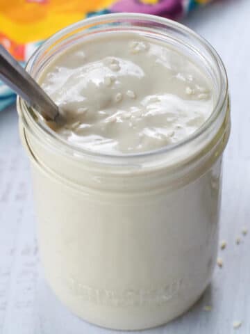 Tahini sauce in a glass jar with a spoon in it