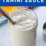 Tahini sauce in a glass jar with a spoon in it