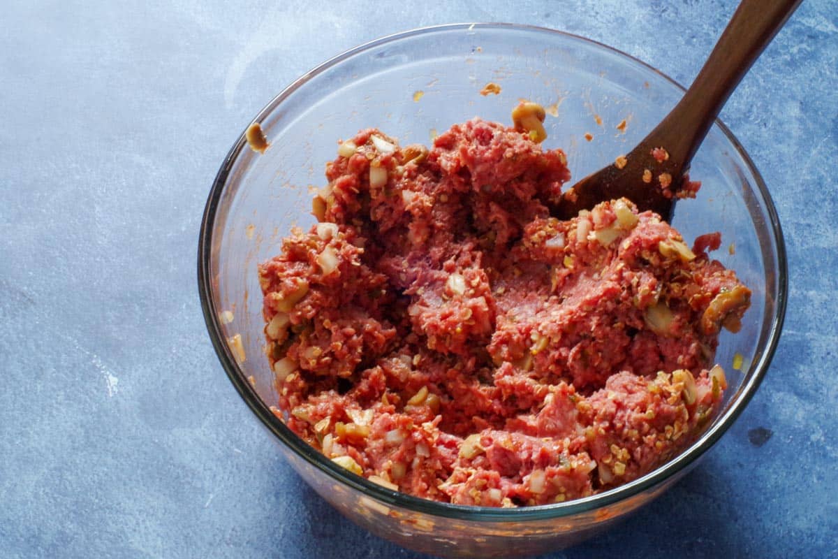 meatloaf ingredients in a large glass mixing bowl with a wooden spoon in bowl