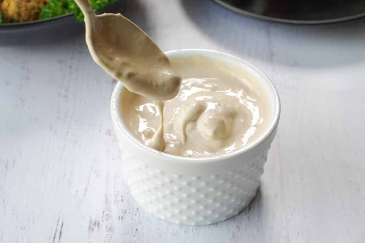 tahini sauce in a white dish with a spoon scooping some out of the dish