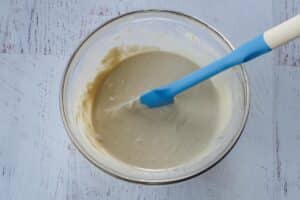 Tahini sauce in a glass bowl with a blue spatula