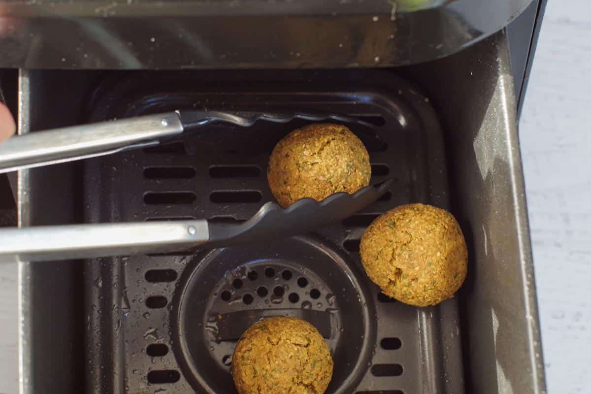 cooked air fryer falafel being removed with silicone tongs