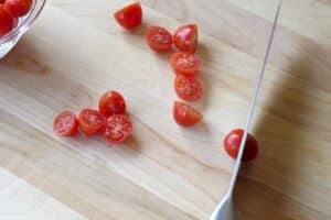 grape tomatoes being cut in half, on wooden cutting board