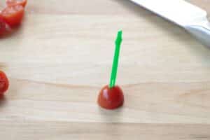½ a grape tomato on wooden cutting board with a skewer through the top of it