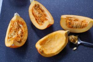 pumpkin cut into quarters with pulp and seeds being scooped out