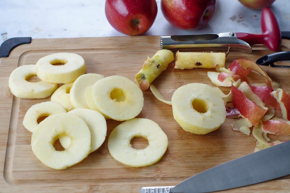 apples peeled, cored and cut into about 3mm circles on cutting board, with corer and knife and peels in background