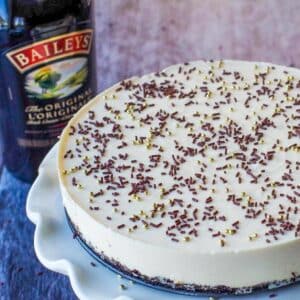Part of a whole No bake Baileys cheesecake on a white cake platter with a bottle of baileys in the background
