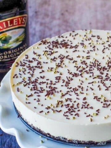 Part of a whole No bake Baileys cheesecake on a white cake platter with a bottle of baileys in the background