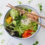 chicken poke bowl with chopsticks laying over the bowl and pea shoots strewn around bowl.