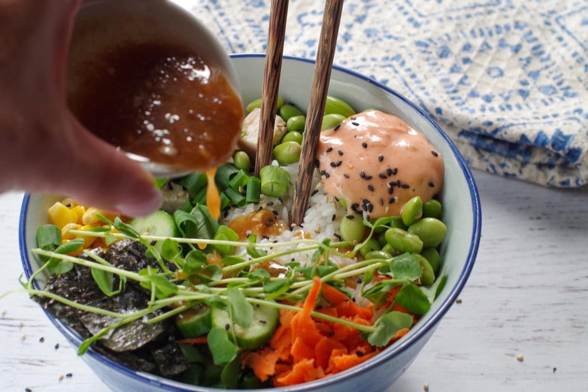miso dressing being poured over chicken poke bowl.