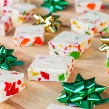 Nougat candy, cut into squares, on a wooden cutting board with green and gold mini bows